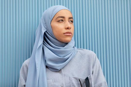 Young lonely Muslim female with melancholic gaze looking away against ribbed wall in daytime