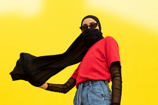 From below of ethnic female in bright casual outfit and headscarf looking at camera during COVID 19 pandemic