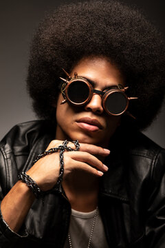 Fashionable African American male in leather jacket and boots sitting on gray background