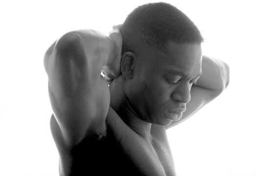 Black and white side view of serious young shirtless athletic African American guy with hands behind back and closed eyes on white background in studio