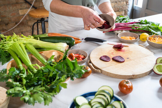 Crop unrecognizable female with fresh beetroot in a bowl with knife while preparing vegetarian lunch in house kitchen