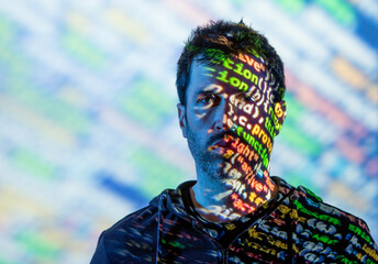 Adult bearded male in hoodie with multicolored words on half of face from projector light looking at camera