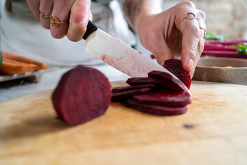 Crop unrecognizable female cutting fresh beetroot with knife while preparing vegetarian lunch in house kitchen