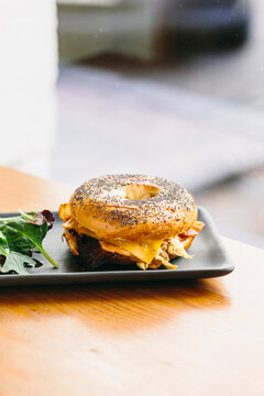 Appetizing bagel sandwich with cheese and chicken served on plate with rucola salad on table in cafe