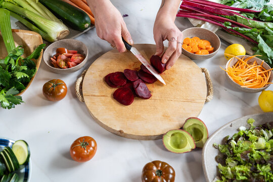 Crop unrecognizable female cutting fresh beetroot with knife while preparing vegetarian lunch in house kitchen