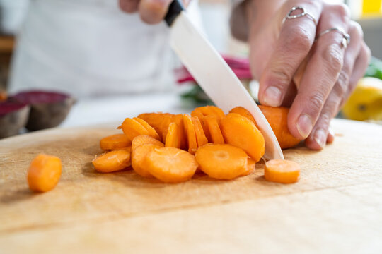 Crop unrecognizable female cutting raw carrot with knife while preparing vegetarian food in house