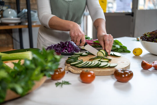 Crop unrecognizable female cutting zucchini with knife while preparing lunch at kitchen table in house