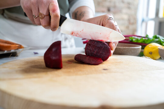 Crop unrecognizable female cutting fresh beetroot with knife while preparing vegetarian lunch in house kitchen