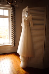 Wedding dress hanging near a window in a dressing room on the morning of a wedding. Getting ready photos in a mansion in Ontario, Canada.