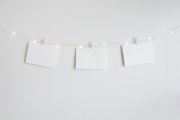 Three horizontal blank cards mockup hanging by small clothespins on an LED light string. Modern and...
