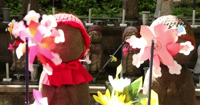 A slow motion of moving colorful windmills with Jizo statue daytime closeup