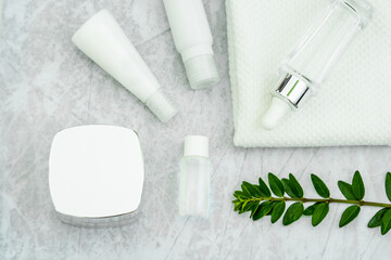 cosmetically flat lay: jars of skin care cosmetics in silver colour, white towel and a sprig of luscious greenery