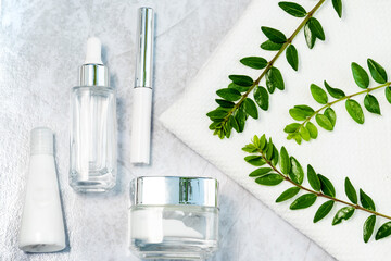cosmetically flat lay: jars of skin care cosmetics in silver colour, white towel and a sprig of luscious greenery