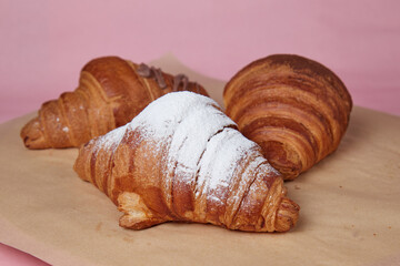 fresh croissants with powdered sugar on the table close-up, blurred background, bread on craft paper