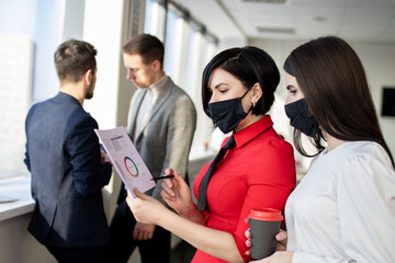 Fototapeta premium Business partners girls in face masks are discussing a project. Coronavirus protection.