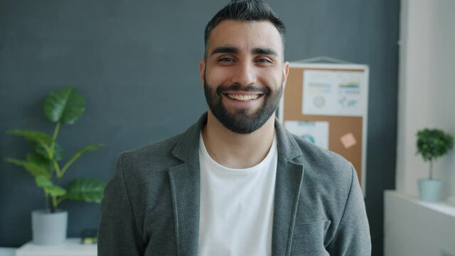 Slow motion portrait of cheerful good-looking entrepreneur standing in office smiling looking at camera with happy face. People and emotion concept.