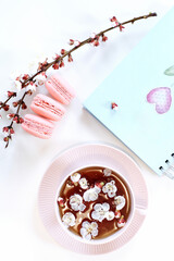 Designer workspace on desk table essential elements on flat lay.White office desk table with blue notebook, pink macaroons, cup of tea with flowers. Top view. Selective focus