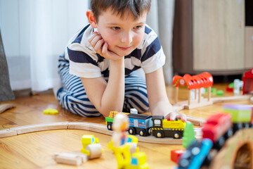 Cute boy is playing with toy railway road at home or in kindergarten on the floor. Child at home or in kindergarten © spyrakot