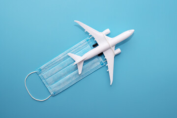 A plane model with a medical mask on a blue background. Safety flight and travel during quarantine...