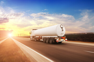 Big fuel tanker truck driving fast on a countryside road against a sky with a sunset