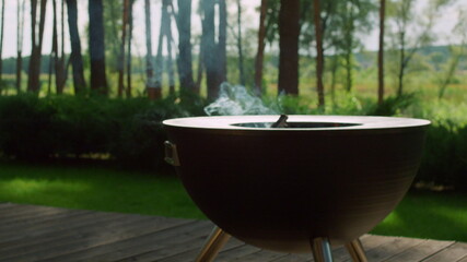 Smoke coming from firewood smolder in bbq grill. Empty grid on backyard