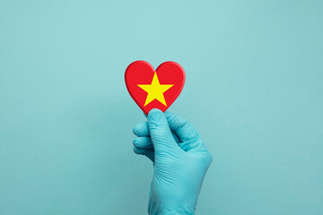 Hands wearing protective surgical gloves holding Vietnam flag heart