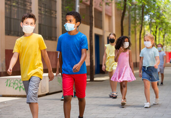 Group of positive children in masks walking together on the street