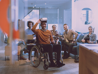 Disabled businessman in a wheelchair at work in modern open space coworking office with team using virtual reality googles drone assistance simulation