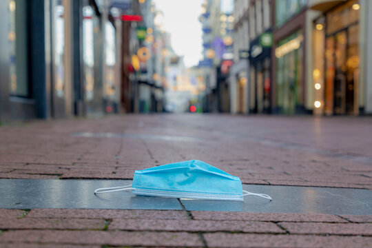 Due to outbreak of coronavirus disease (COVID-19) scourge, Second lockdown in Netherlands, Used of blue surgical face mask on the ground floor with blurred shopping street Kalverstraat, Amsterdam.