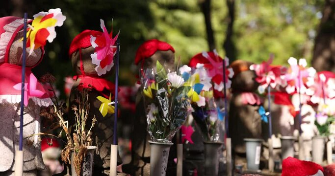 A slow motion of moving colorful windmills with Jizo statue daytime closeup