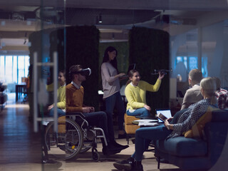 Fototapeta na wymiar Disabled businessman in a wheelchair at work in modern open space coworking office with team using virtual reality googles drone assistance simulation