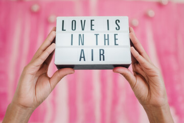 Hands holding a light box with Love is in the air message