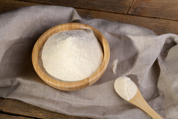 Whole wheat durum flour on a scooped wooden spoon and in wooden bowl with spikelets on a natural wooden background