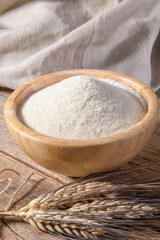 Whole wheat durum flour in wooden bowl with spikelets on a natural wooden background, close up
