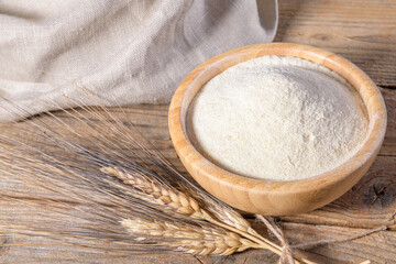 Whole wheat durum flour in wooden bowl with spikelets on a natural wooden background, close up