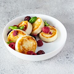 Fresh cottage cheese or ricotta  pancakes (syrniki,fritters) on a white plate with fresh berries and jam. Delicious healthy cottage cheese breakfast.  Ukrainian, Russian cuisine sweet food