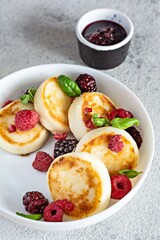 Fresh cottage cheese or ricotta  pancakes (syrniki,fritters) on a white plate with fresh berries and jam. Delicious healthy cottage cheese breakfast.  Ukrainian, Russian cuisine sweet food