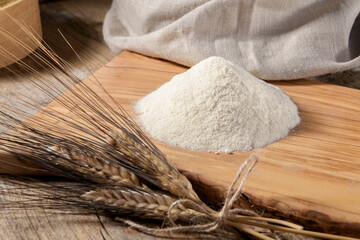 Wheat flour on a wooden cutboard and spikelets on a wooden table, close up