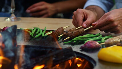 Unrecognizable man turning kebab outside. Unknown guy cooking meat on sticks