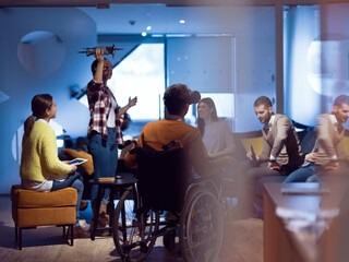 Disabled businessman in a wheelchair at work in modern open space coworking office with team using virtual reality googles drone assistance simulation