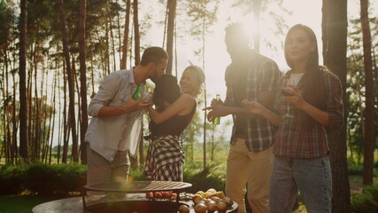 Cheerful friends dancing on bbq party in forest. Woman holding dog outdoors