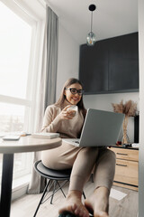 Beautiful happy woman working at home with laptop taking cup of coffee . Smiling business woman woman wearing eyeglasses in office,  using laptop computer