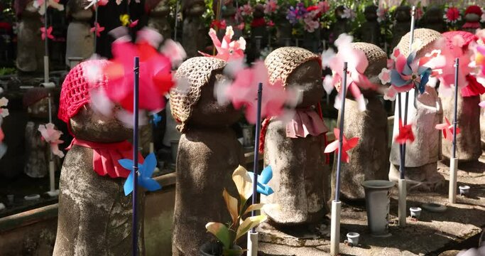 A slow motion of moving colorful windmills with Jizo statue daytime
