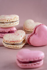A group of heart-shaped French macaron cookies, vanilla and strawberry flavour, copy space on a pink fabric background