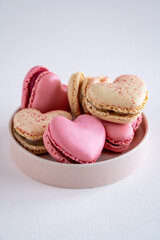 A group of heart-shaped French macaron cookies on round plate, vanilla and strawberry flavour, copy space on neutral background