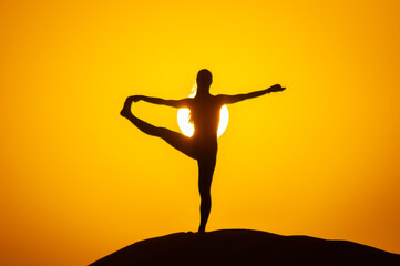 Silhouette of a young woman doing yoga pose at sunset