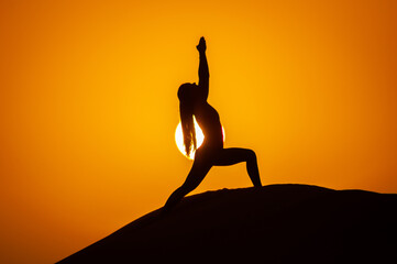 Silhouette of a young woman doing yoga pose at sunset