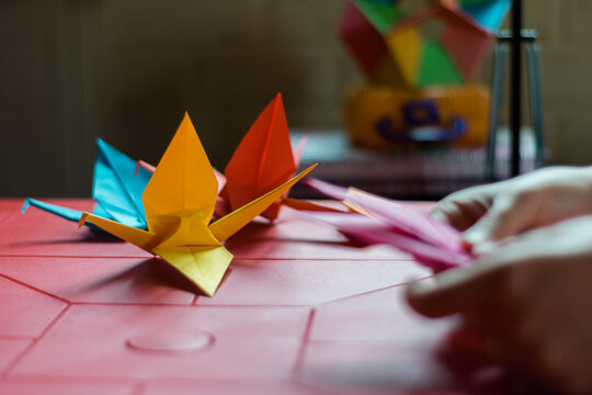 colored cranes on a red plastic table and hands making another crane