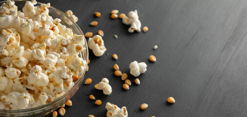 Maíz palomero y palomitas en un recipiente, tiradas sobre la mesa de color negro vintage