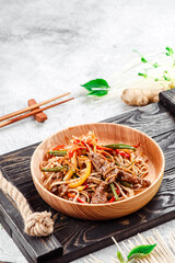 Pan-Asian food. Noodles with vegetables, shiitake mushrooms and meat in wooden plate on a concrete background. Space for text